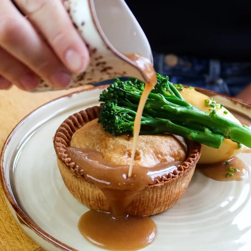 Gravy poured over a shortcrust pie with tenderstem broccoli and mash